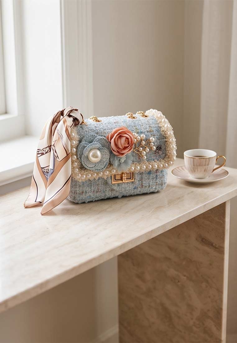 Schmuckzauber Tweed Trachtentasche Glamour hellblau im Frontansicht. Die Tasche ist hellblau und verfügt über eine Perlapplikation und eine kleine Seidenschleife.