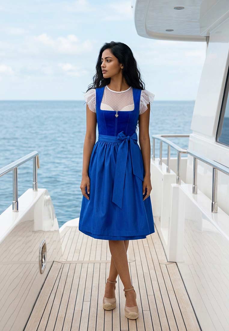 Marjo Dirndl Zoey blau: Frontansicht einer Frau in einem blauen Dirndl mit schmalem Bund und Schleife, sowie einem transparenten Oberteil mit Pünktchenmuster und kurzen Puffärmeln.
