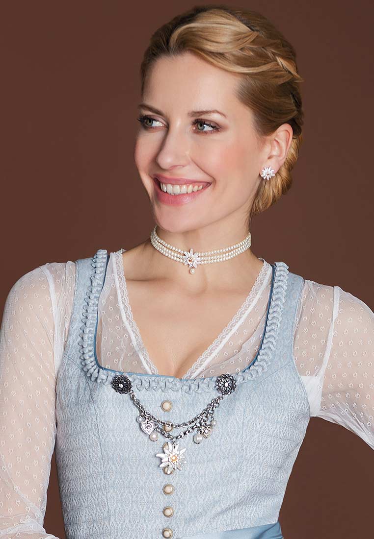 Alpenflüstern Perlen-Kropfkette Greta, Frontansicht einer Frau in hellblauer Tracht, die eine Halskette aus Perlen und einem Anhänger trägt.