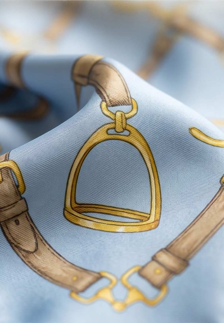 Detailansicht eines hellblauen Schmuckzauber Nickituch Timeless mit einem stilvollen Pferdezaumzeug-Muster in Gold und Braun.
