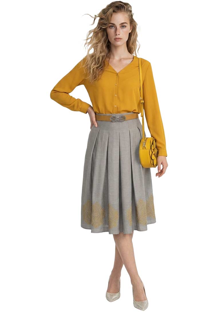 Frontansicht einer Frau, die eine senfgelbe Langarm-Trachtenbluse Aline von byoung mit einem grauen Faltenrock und silbernen Pumps trägt.
