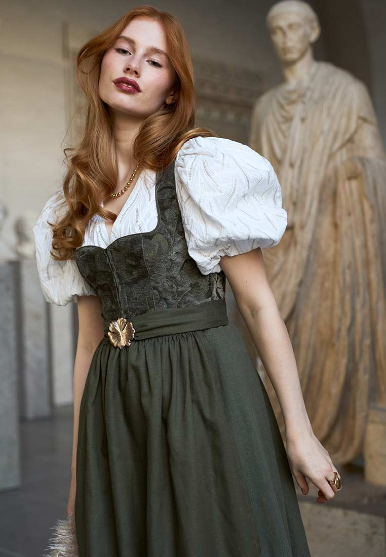 Madame Marie Dirndl Velirina Samt thymian 75 cm, Frontansicht. Elegantes grünes Samtdirndl mit puffärmeligem weißem Oberteil und sichtbarem Taillengürtel mit Brosche.