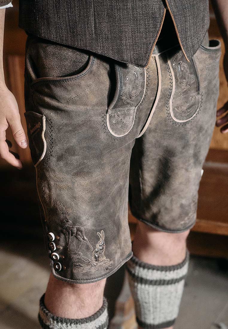 Krüger Lederhose Lebenslang mit Gürtel braun, Frontansicht. Hochwertige Lederhose in Braun mit seitlichen Taschen und dekorativen Knopfleisten am Beinabschluss.