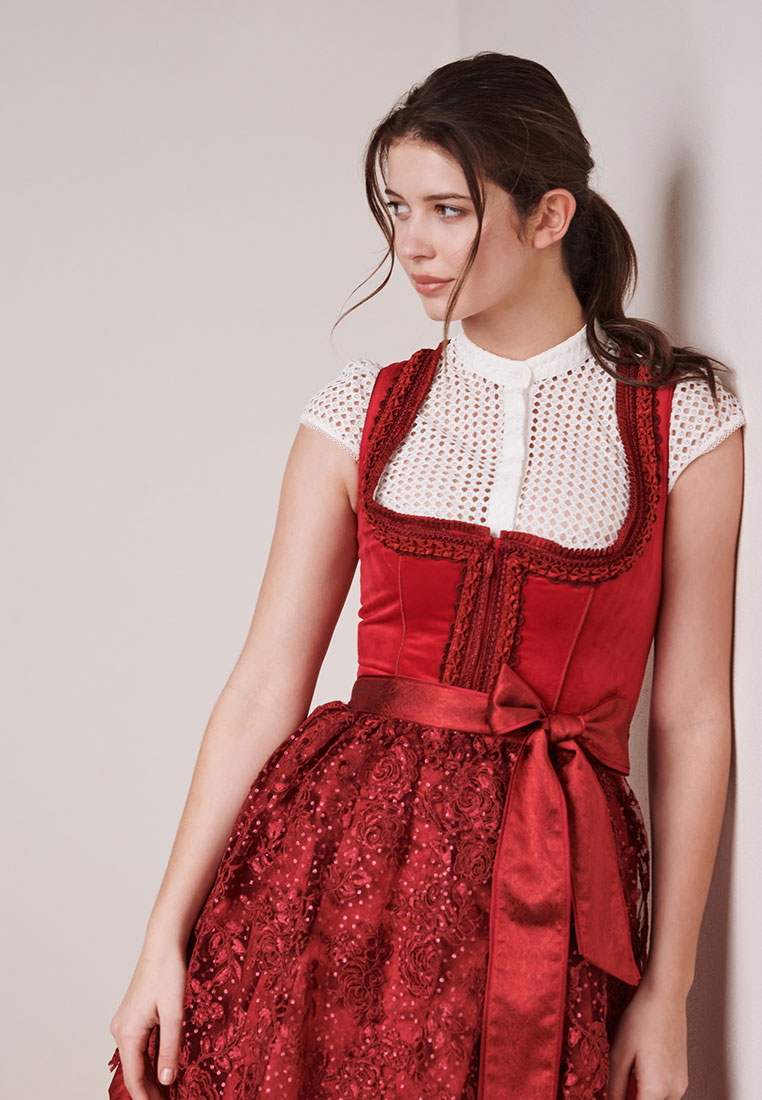 Krüger Dirndl Elma rot in roter Farbe, Seitenansicht. Das Modell zeigt einen V-Ausschnitt mit Spitzenbesatz und eine Schnürung vorne. Der Rock ist aus Spitzenstoff gefertigt.