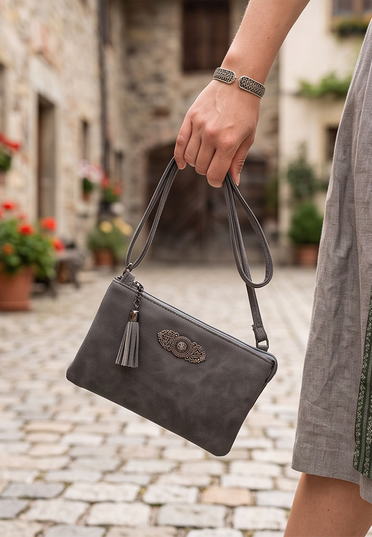 Taschenzauber Trachtentasche Marie dunkelgrau, Frontansicht einer dunkelgrauen Tasche mit Fransenanhänger und Zierapplikation, gehalten von einer Hand.