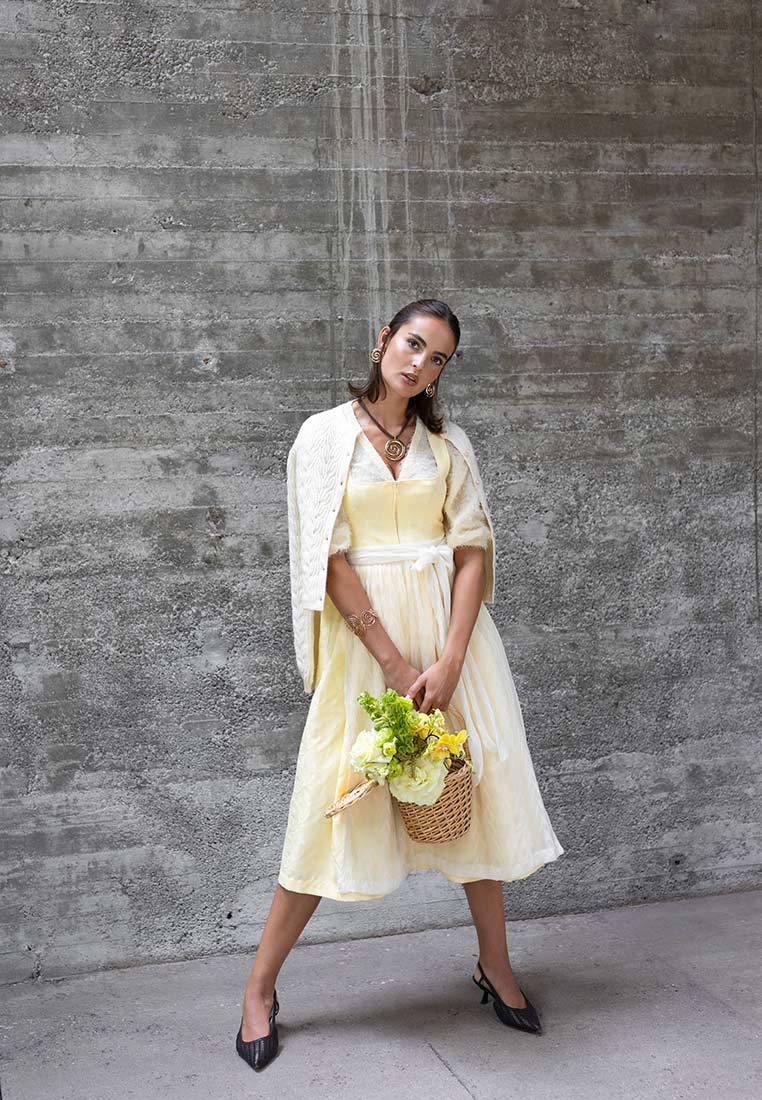 Madame Marie Trachtenstrickjacke Avenara cremeweiss: Frontansicht einer Frau in einer cremeweißen Strickjacke mit Zopfmuster und langen Ärmeln.