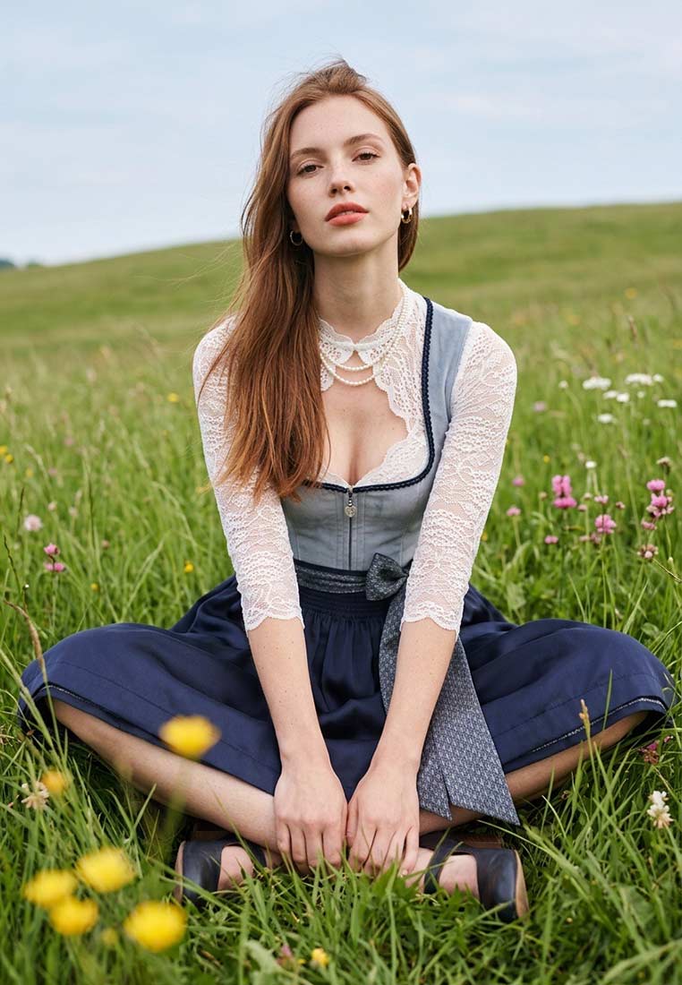 Krüger Dirndl Dena blau, Frontansicht. Das traditionelle Dirndl ist aus dunkelblauem Stoff gefertigt und kombiniert mit einer hellblauen Schürze und einer weissen Spitzenbluse.