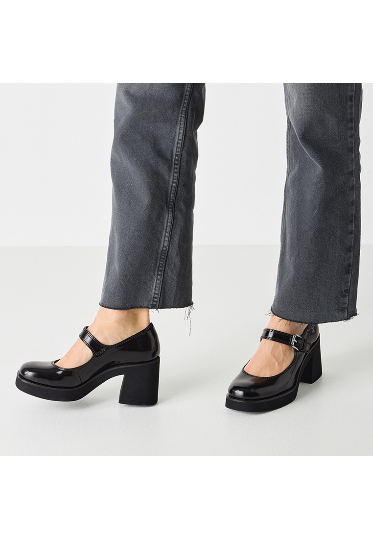 Tamaris Mary Jane Pumps schwarz: Frontansicht von zwei schwarzen Lack-Pumps mit Blockabsatz und Riemchen, getragen mit dunklen Jeans.
