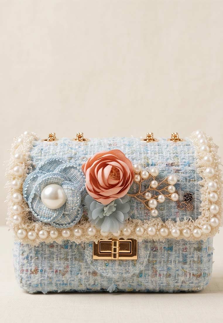 Schmuckzauber Tweed Trachtentasche Glamour hellblau: Frontansicht einer kleinen, hellblauen Tasche mit Perlenrand und Stoffblumen-Applikationen.