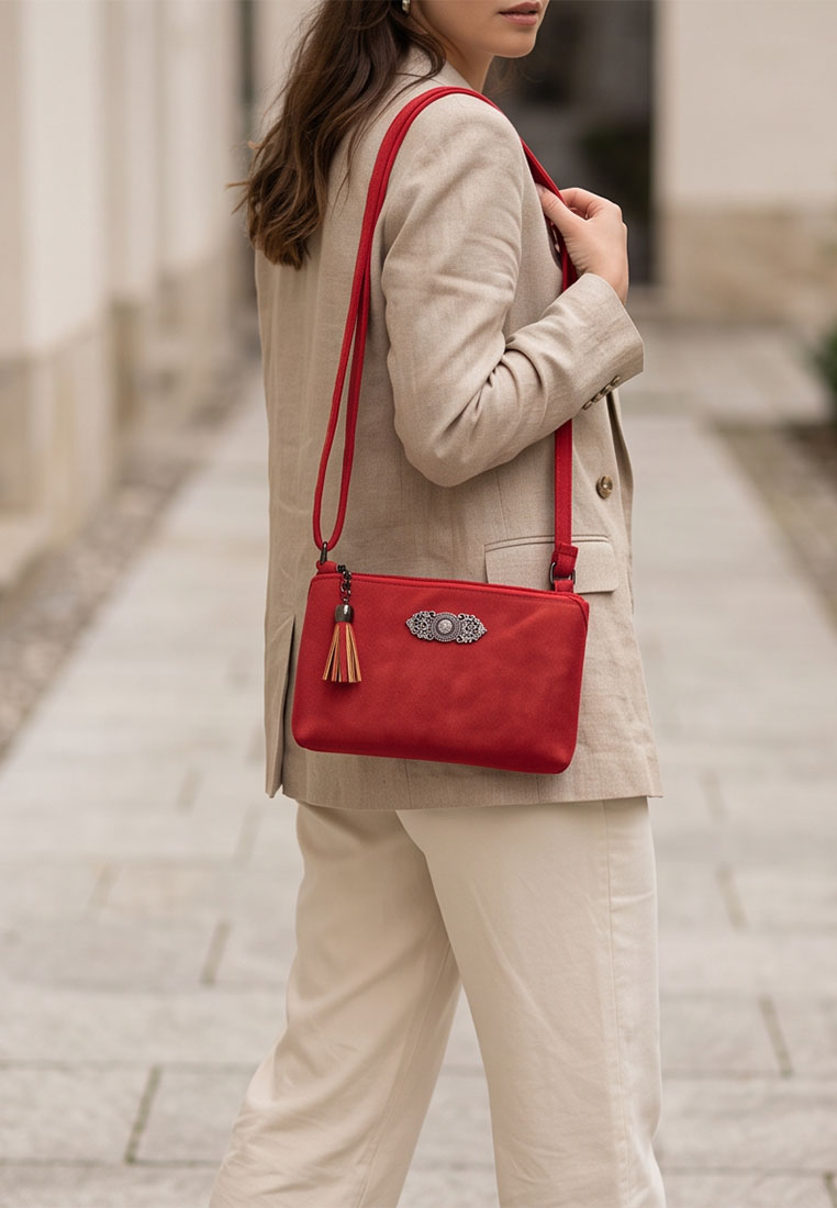 Taschenzauber Trachtentasche Marie rot: Frontansicht der roten Tasche mit Quaste und Schmuckdetail, getragen über der Schulter zu einem beigefarbenen Blazer und hellen Hosen.
