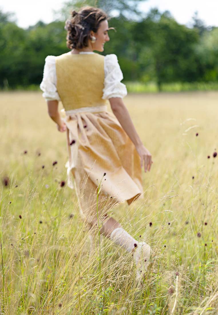 Marjo Dirndl Wolfersdorf in Safrangelb mit 65 cm Rocklänge in der Frontansicht, kombiniert mit einer weissen Bluse. Das Dirndl hat ein gelbes Oberteil und einen Rock.