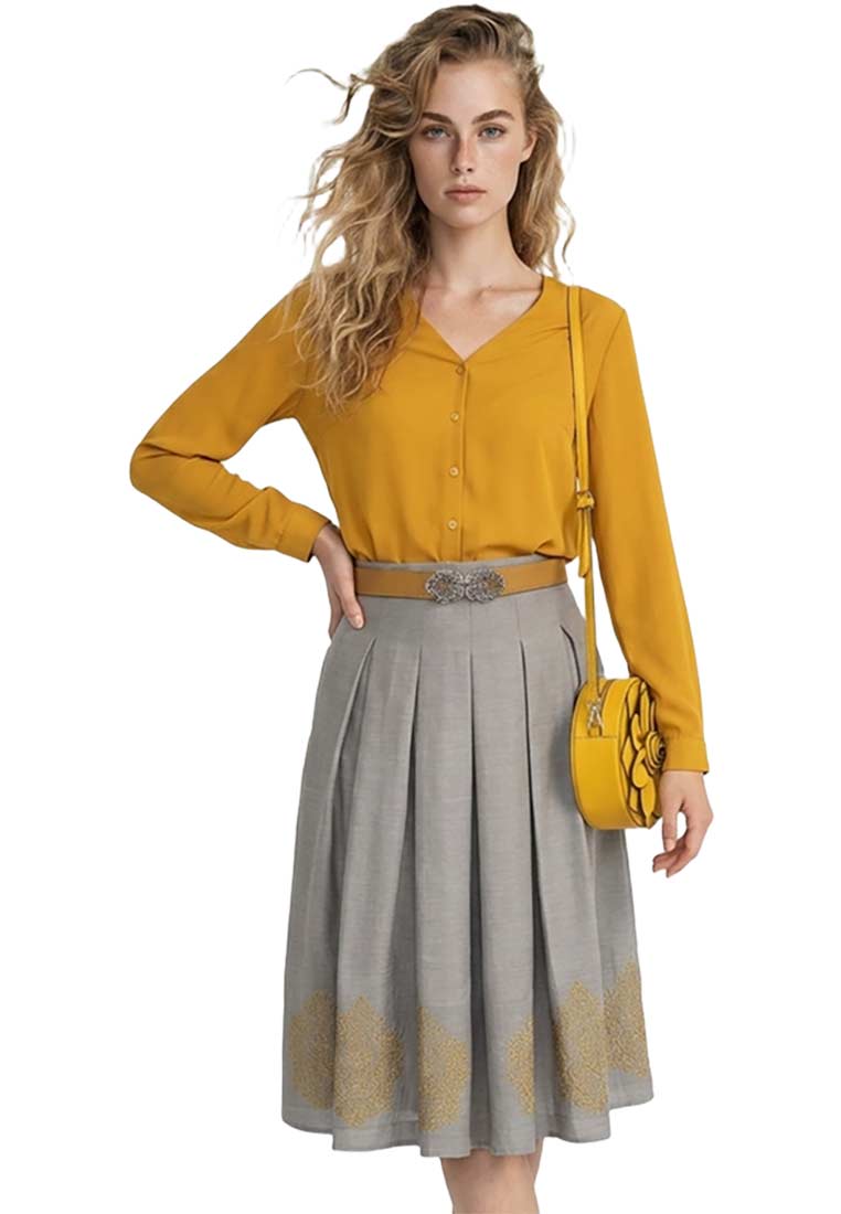Kaiseralm Trachtenrock Herlind in Grau, Frontansicht mit Falten und goldener Stickerei am Saum, getragen mit einem senfgelben Oberteil und einer runden Handtasche.