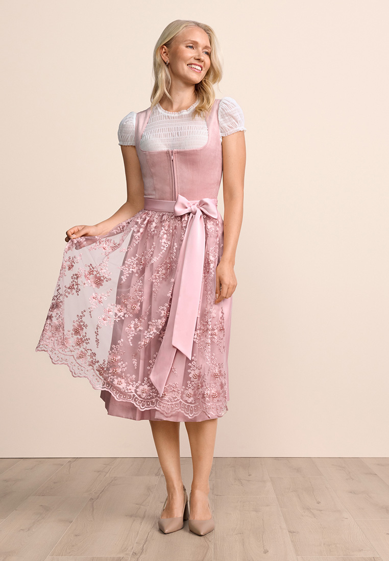 Krüger Dirndl Lovira rosa 60cm in Frontansicht. Das Kleid ist rosa und mit einem aufwendigen Blumenmuster verziert, mit einer farblich passenden Schürze und einem Reissverschluss vorne.