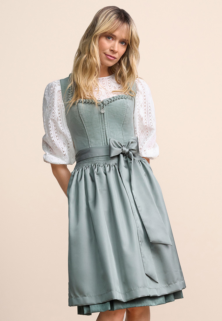 Frontansicht eines Krüger Dirndl Ariella in Türkis mit 60cm Rocklänge, das mit einer weißen Bluse kombiniert wird. Der Dirndl-Oberteil ist aus Cord gefertigt und mit einer Schleife am Rockbund verziert.