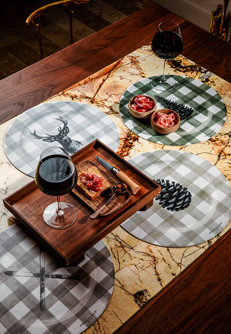 Pôdevache Platzteller Ø38 im Chalet Chic Stil, Stimmungsbild mit karierten Sujets Tanne, Tannenzapfen und Hirsch, dekorative Tischszene zur Präsentation der Designs.