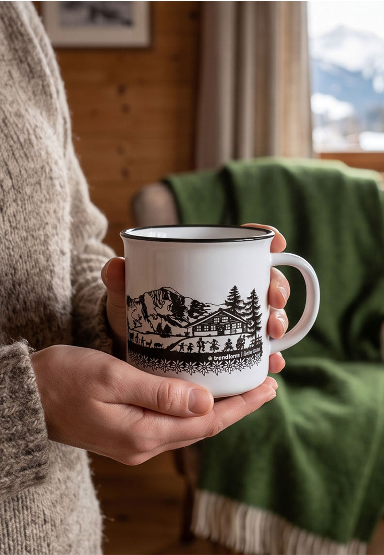 Trendform Keramik Tasse SWISS TRADITION, Frontansicht, weiß. Die Tasse zeigt eine schwarze Illustration von Bergen, einer Hütte und Silhouetten von Menschen und Tieren.