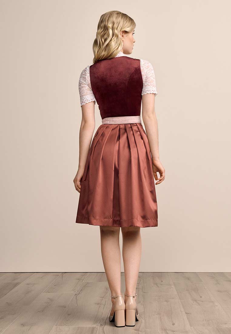 Krüger Dirndl Aurela bordeaux 60cm, Rückansicht. Ein stilvolles Dirndl in Bordeaux mit einem Samtmieder und einem satinartigen Rock mit Falten. Der weiße Spitzenkragen des Unterhemds ist sichtbar.
