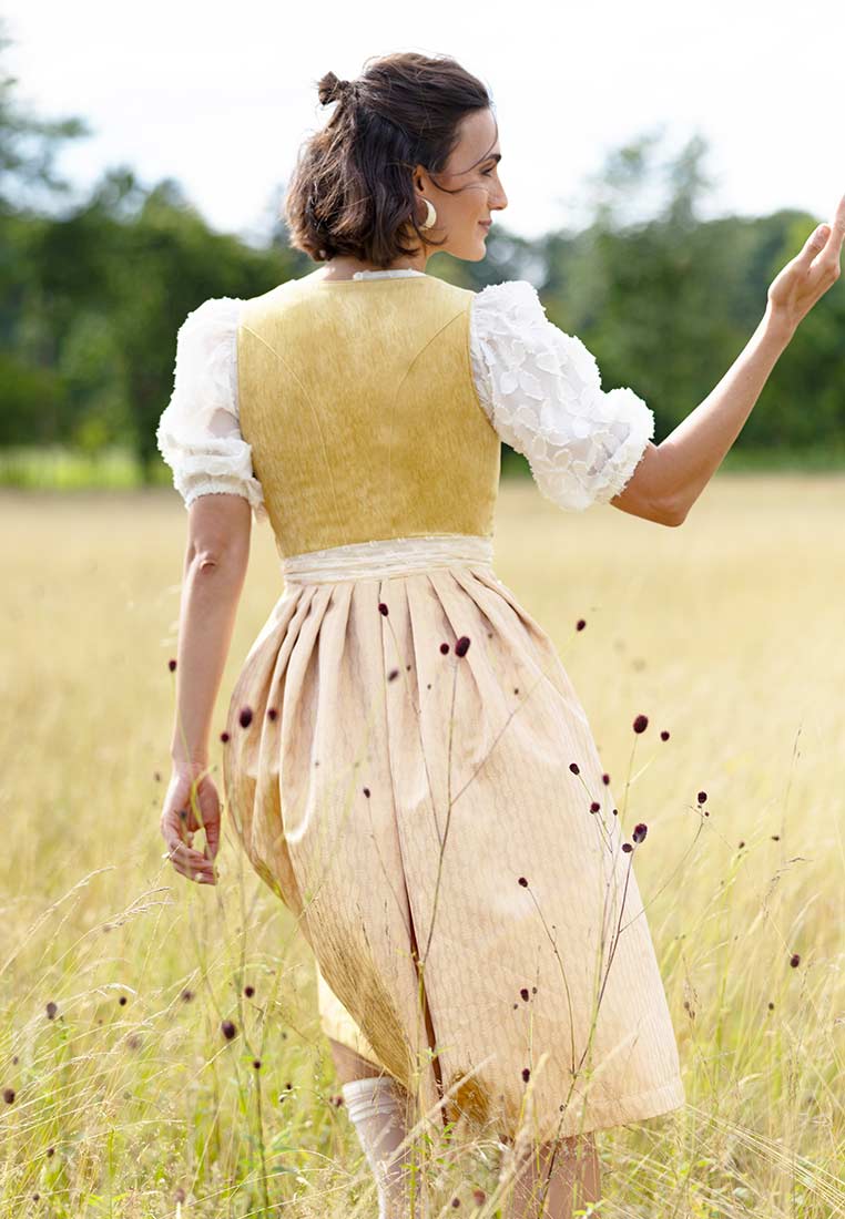 Marjo Dirndl Wolfersdorf safrangelb 65 cm: Rückansicht eines safrangelben Dirndls mit beige gemustertem Rock und weißer Bluse mit Puffärmeln.