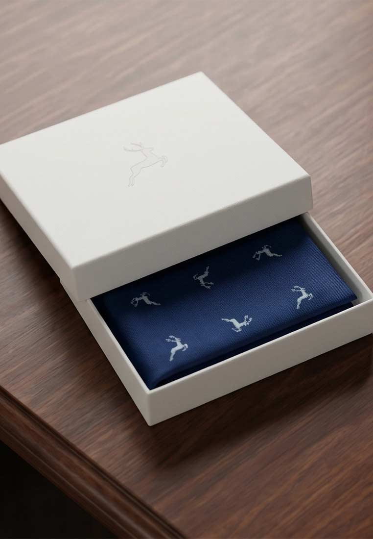Luise Steiner Stecktuch Lois marine himmel in einer geöffneten weißen Box, Frontansicht, mit hellem Hirschmuster auf marineblauem Hintergrund.