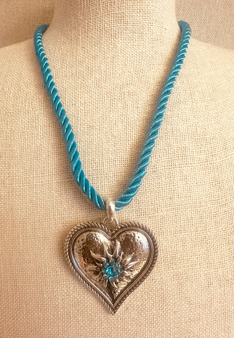 Kordelkette in türkis mit einem silbernen Herzanhänger und kleinen türkisen SGlitzersteinen in der Mitte eines Edelweisses. 