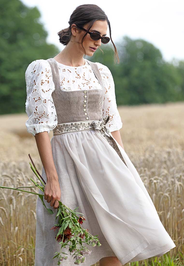 Marjo Dirndl Leopoldsdorf taupe 65 cm, Frontansicht. Das modische Dirndl in Taupe hat eine helle Schürze und eine weiße Bluse mit Spitzenärmeln.