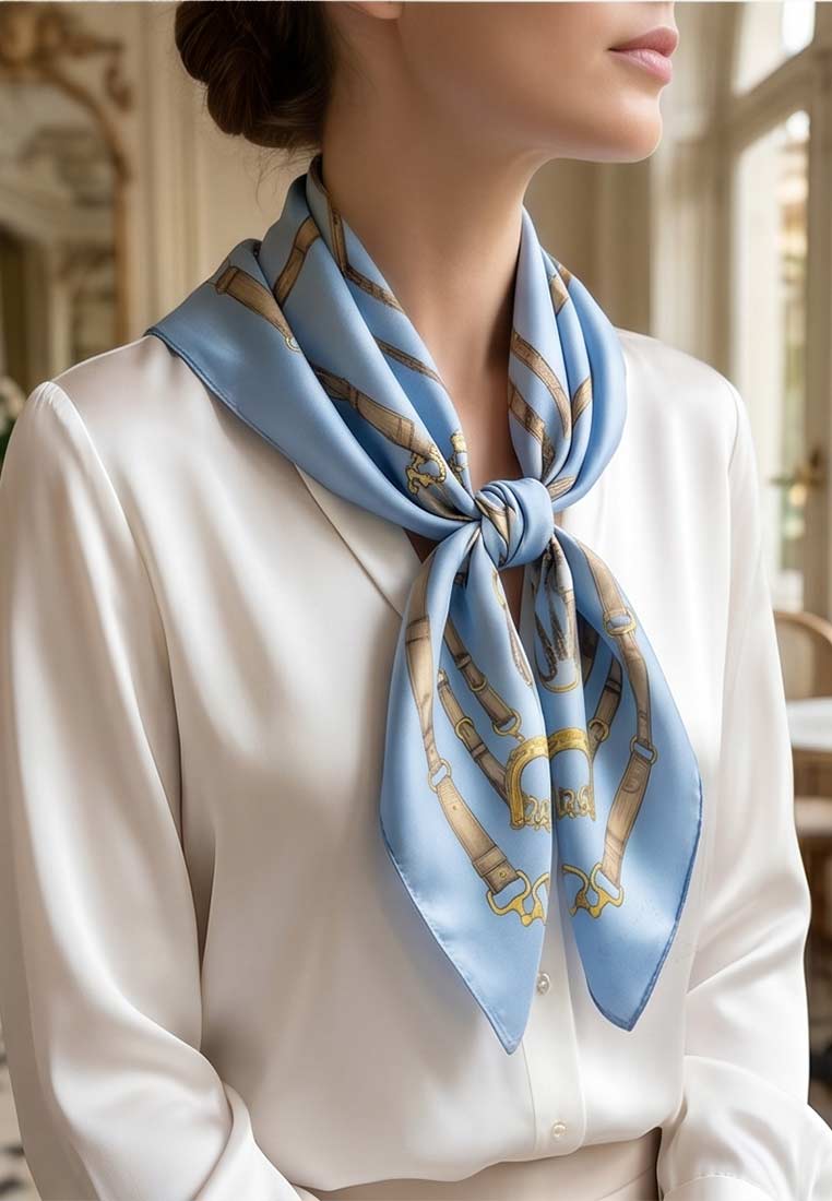 Schmuckzauber Nickituch Timeless hellblau aus Seide mit Pferdegeschirr-Muster, Frontansicht. Das elegante Tuch ist hellblau mit einem Muster aus braunen Lederriemen und goldenen Schnallen.