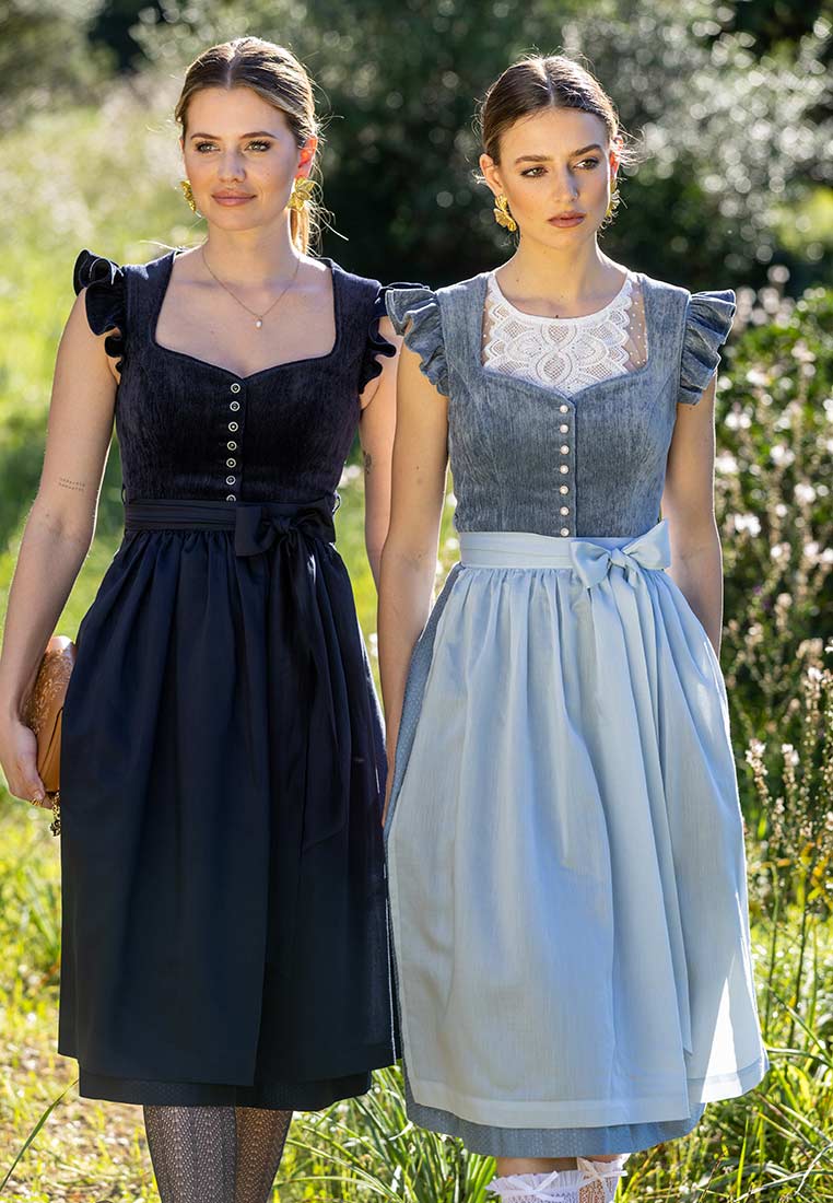 Zwei Frauen in Tracht vor einer grünen Kulisse. Frontansicht des MarJo Trachten Dirndl Hochwinkel himmelblau 65 cm in Hellblau mit Knöpfen und Schürze.
