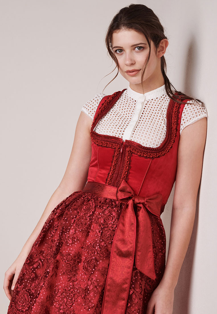 Krüger Dirndl Elma in Rot: Frontansicht eines stilvollen roten Dirndls mit einem Spitzenoberteil und einem verzierten Rock, vorne mit Schleife gebunden.