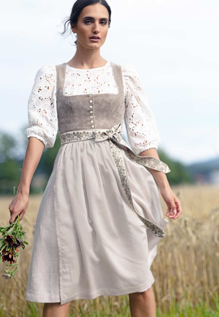Marjo Dirndl Leopoldsdorf taupe 65 cm Frontansicht eines traditionellen Dirndls in Taupe mit einer weissen Bluse mit Spitzenärmeln, geschnürt mit einem gemusterten Band.